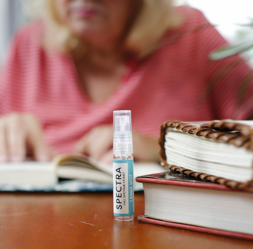 A container of Spectra Cannamist spray in the foreground with an older woman in the background. 