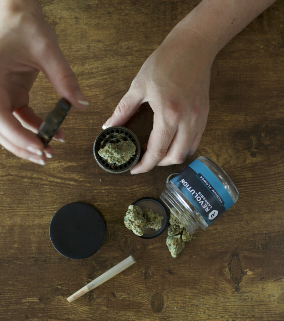 cannabis flower in the grinder with the jar and a joint on a table.