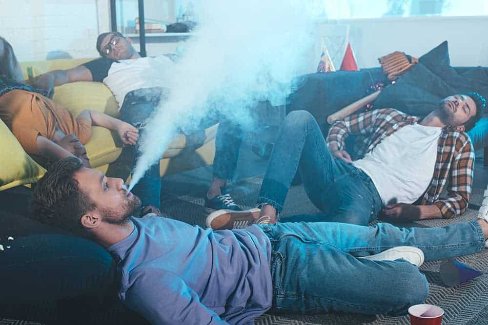 Three young men smoking and laying around in a messy living room.