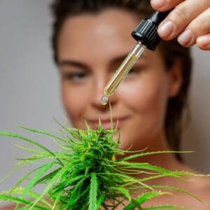 A young woman with a dropper full of CBN oil dripping onto hemp flower.